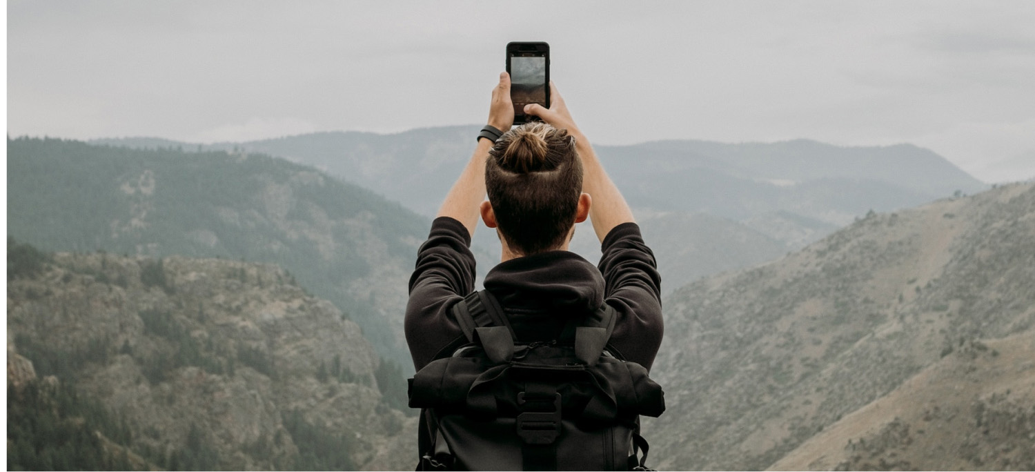 Man holding up phone in mountain landscape